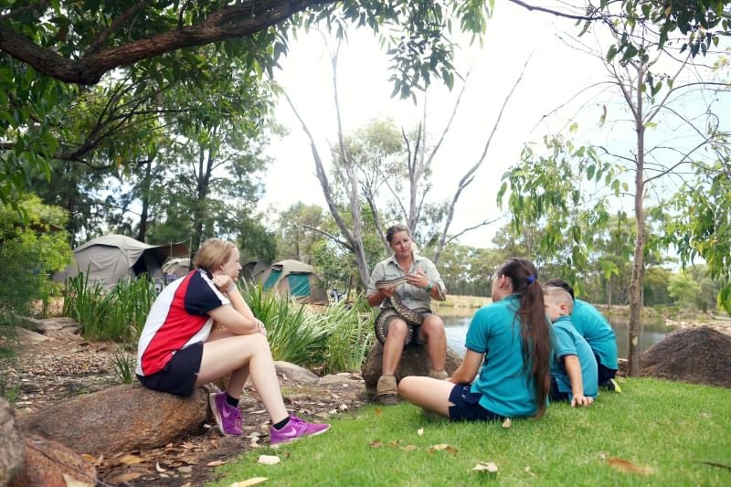 A small group of students with Taronga educator sitting on rocks in outside learning space at Taronga Western Plains Zoo